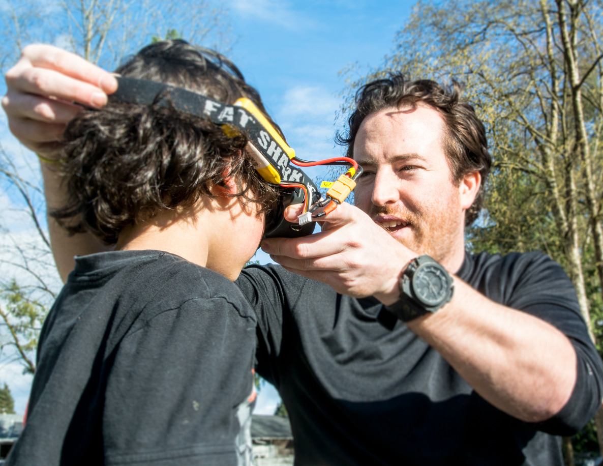 Instructor fitting FPV goggles on a student during a hands-on drone training session