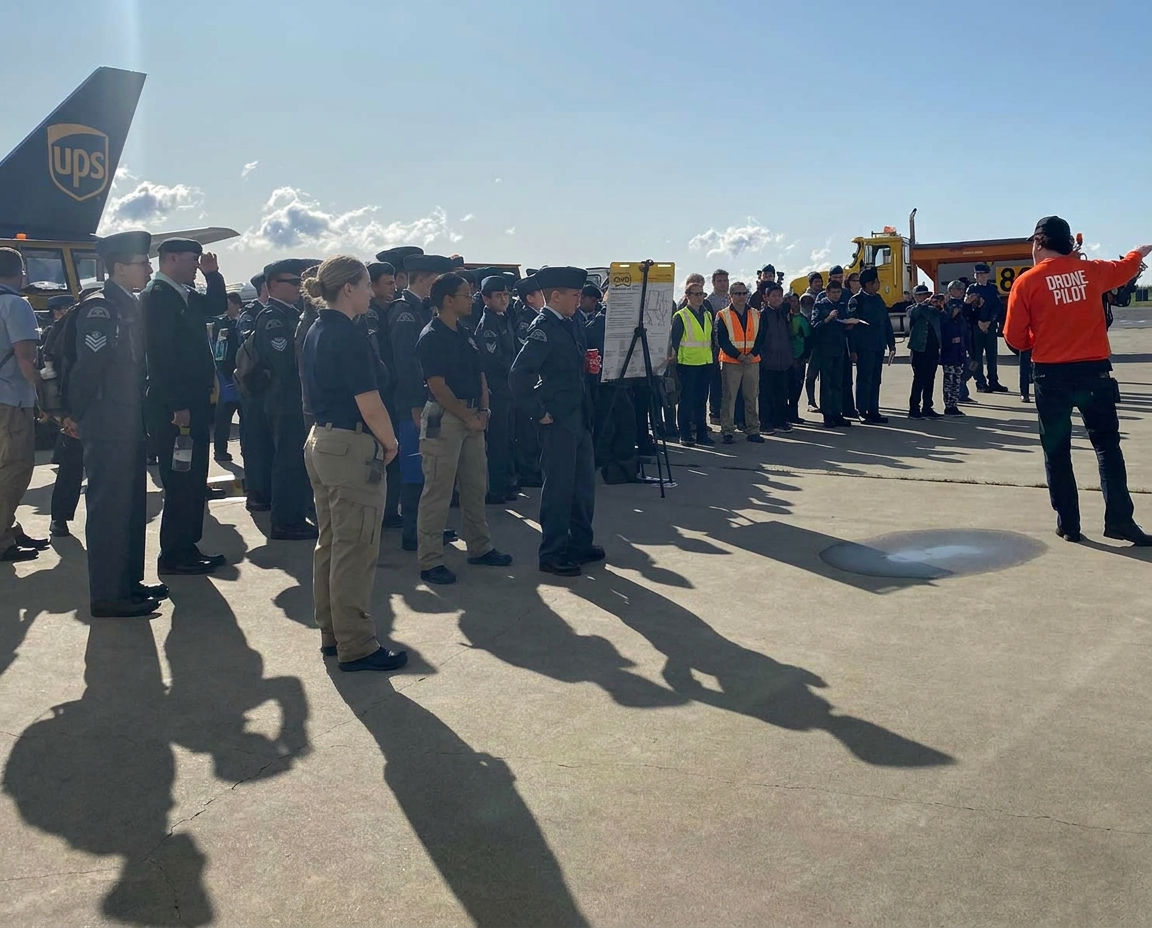 Drone pilot instructor briefing a large organized group of cadets and trainees on an airport apron